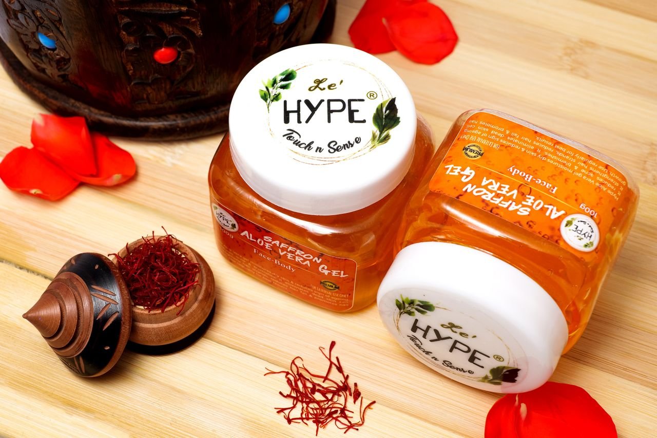 Close-up of saffron aloe vera gel jars with decorative saffron threads and petals on a wooden surface.